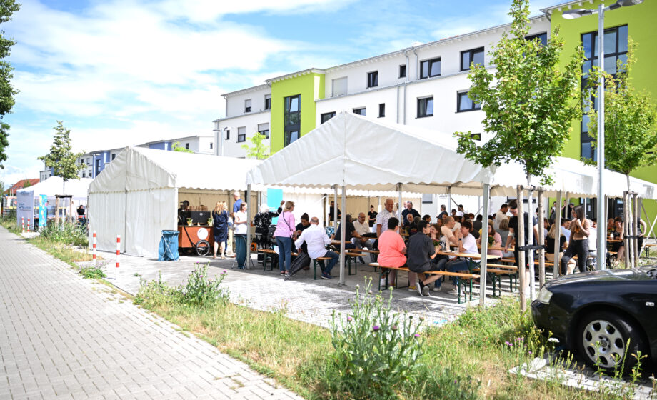 Leute sitzen vor einer Wohnsiedlung zusammen auf Bänken und unterhalten sich