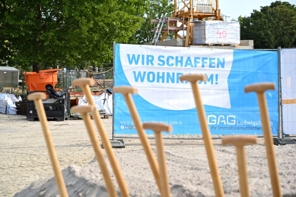 Man sieht die Stiele von Spaten vor einem Bauzaunbanner