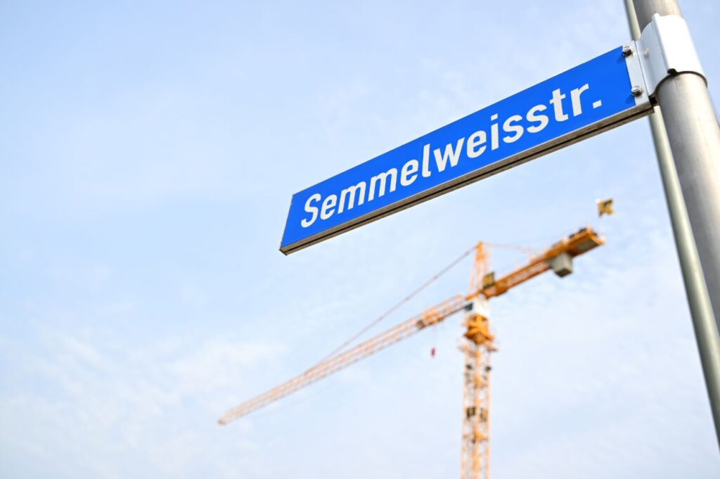 Man sieht ein Straßenschild mit der Aufschrift "Semmelweisstraße" vor einem Kran